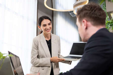 Selective focus at computer screen. Caucasian business women dress in formal suit holding laptop computer while meeting about work project to boss with smile and confident.  indoor office work shot.の写真素材