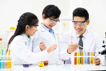 Young Asian kids wearing white scientist gown and do chemical test tube while study, learning in science classroom with teacher. Young children education concept by experiment, fun and enjoy classroomの写真素材