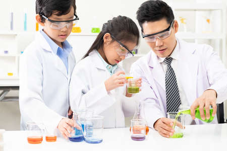 Young Asian kids wearing white scientist gown and do chemical test tube while study, learning in science classroom with teacher. Young children education concept by experiment, fun and enjoy classroomの写真素材