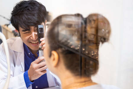 Selective focus at Optometrist face. While doctor using penlight and subjective refraction to  examine eye visual system of elder patient women with professional machine before made glasses.の写真素材