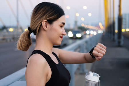 Selective focus at face of young beautiful Asian women using smart watch to track activity and listen music while warm up before exercise or running at the urban city view. Fit and healthy lifestyle.の写真素材