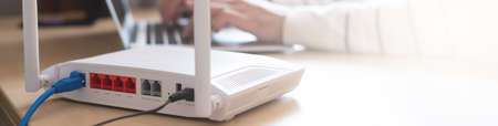 à¸ºà¸ºBanner horizontal shot of Internet router on working table with blurred man connect the cable at the background. Fast and high speed internet connection from fiber line with LAN cable connection.の写真素材