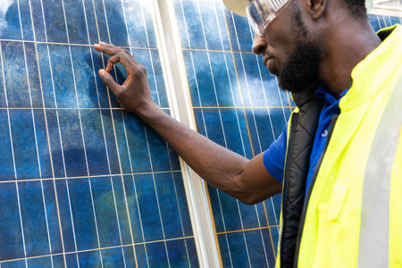 Outdoor shot of black African engineer inspect electrical solar panel wearing hardhat , protective...