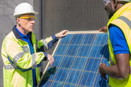 Selective focus at engineer face. African and Caucasian engineer inspect electrical solar panel at building construction site. Alternative energy and industrial concept. Outdoor shot.の写真素材
