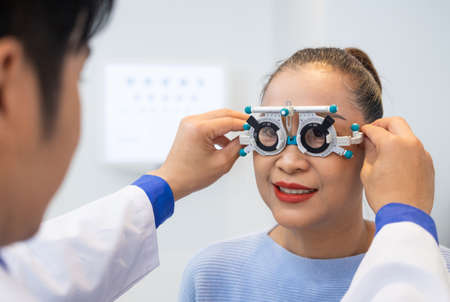 Selective focus at women face. While doctor using Optometry equipment and trial glasses frame  to examine eye visual system of elder patient women with professional machine and technic.の写真素材