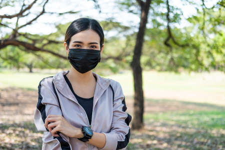 Selective focus at face of young beautiful Asian women wearing surgical face mask using smart watch to track activity before exercise or running at the park in the morning. New normal lifestyle.の写真素材