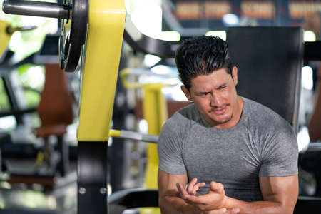 Young adult Caucasian men feeling painful from shoulder muscle injury after workout with weight lifting machine inside of fitness gym. Muscle injured from workout or exercise for weight training.の写真素材