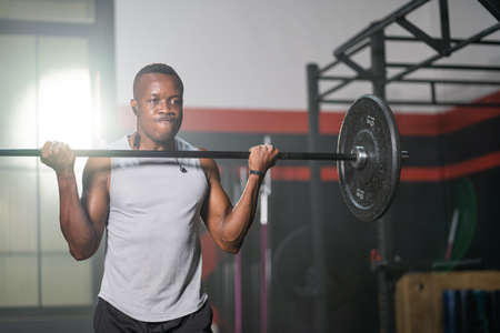Strong adult black African men lift barbell to do crossfit exercise and weight lifting inside of fitness gym to workout for body strength and firm arms muscle and good physical body health.の写真素材