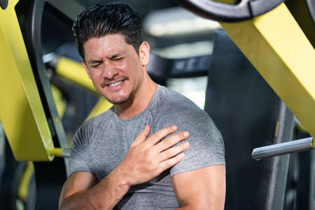 Young adult Caucasian men feeling painful from shoulder muscle injury after workout with weight lifting machine inside of fitness gym. Muscle injured from workout or exercise for weight training.の写真素材
