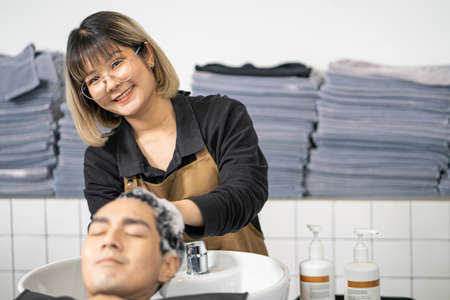 Selective focus at Young Asian women hairdresser while wash hair shampoo and treatment with her client. Hair salon studio with hair stylish, beauty and fashion concept.の写真素材