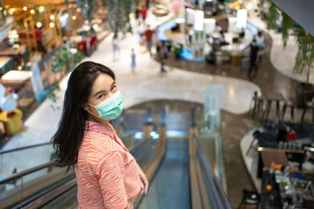 Adult Asian women wearing surgical face mask using mobile phone in department store.