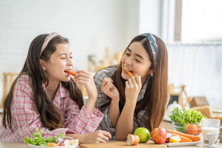Mixed race girl younger and older sister talk and smile while play with each other inside of the kitchen in the morning while ear breakfast. Family relationship, bond, love and togetherness concept.の写真素材