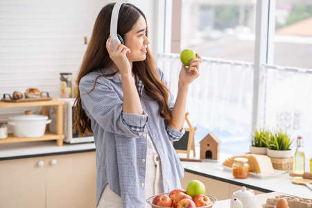 Young Asian women wake up in the morning and eat fresh fruit for breakfast in the kitchen with different type of salad vegetable and healthy food. Good nutrition eating human body condition.の写真素材