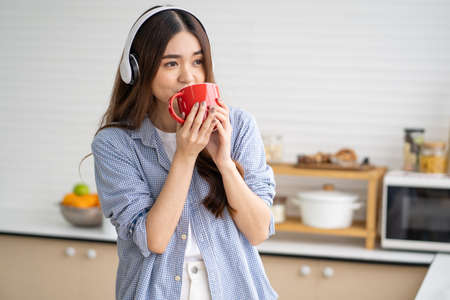 Young Asian women wake up in the morning and drink coffee from hot cup for breakfast in the kitchen with different type of salad vegetable and healthy food. Good nutrition, relaxation.の写真素材