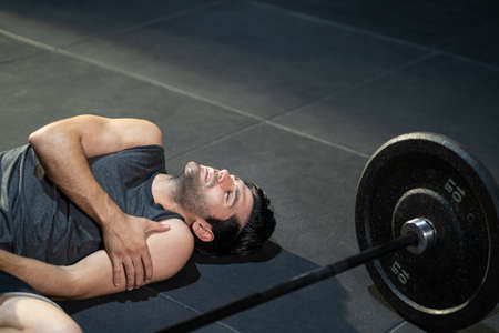 Young adult Caucasian men feeling painful from shoulder muscle injury after workout with weight lifting machine inside of fitness gym. Muscle injured from workout or exercise for over weight training.の写真素材