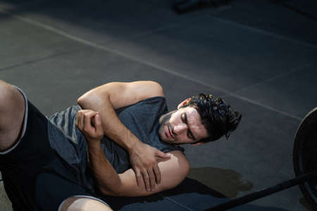 Young adult Caucasian men feeling painful from shoulder muscle injury after workout with weight lifting machine inside of fitness gym. Muscle injured from workout or exercise for over weight training.の写真素材
