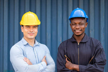 Caucasian supervisor and African men worker standing with arm crossed while inspect the condition of all containers shipment, People and worker in freight deliver, import and export teamworkの写真素材