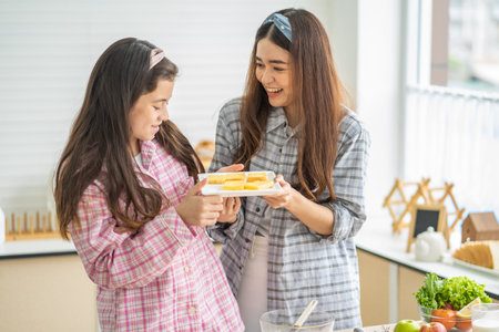 Mixed race girl younger and older sister talk and smile while play with each other inside of the kitchen in the morning while ear breakfast. Family relationship, bond, love and togetherness concept.の写真素材