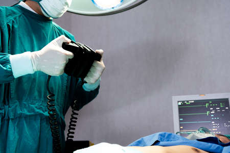 Selective focus at defibrillator while doctor use it to pump at chest of unconscious with low heart rate patient to save life while doing medical surgery inside of operating room. Emergency aid, CPR.の写真素材
