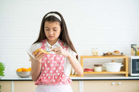 Young Caucasian girl wearing pajamas while put yam spread on the bread for breakfast inside of the modern kitchen. Lifestyle, healthy food concept.の写真素材