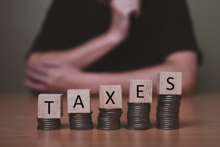 Selective focus at wood tax sign on top of decrease stack of money on the white copy space background. Business or personal tax payment, expense that need to manage and plan.の写真素材