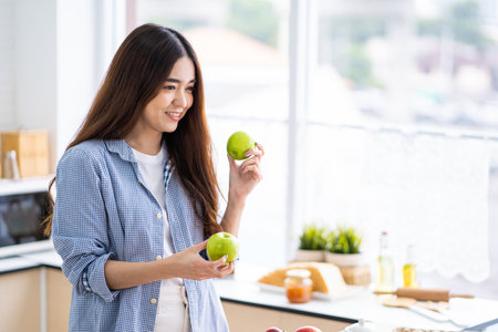 Young pretty Asian women choose fruit and apple for her breakfast inside of the kitchen. Good food with nutrition for healthy eating or diet for weight control.の写真素材