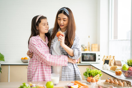 Indoor shot of young sister, teenager playing with each other while eating apple fruit and vegetable inside of the kitchen. Family relationship moment, Diet and good nutrition food.の写真素材