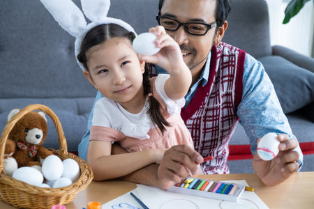 Father and his daughters are painting eggs with colors inside of the living room. Family preparing...