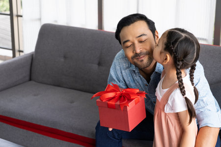 Child Asian girl give a present to his dad while smile, hug and kiss inside of the living room. Happy moment with male parent, family relationship. Father dayの写真素材