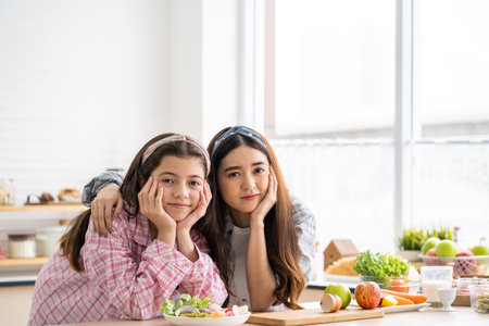 Younger and older sister talk and smile while play with each other inside of the kitchen in the morning while ear breakfast. Family relationship, bond, love and togetherness concept.の写真素材