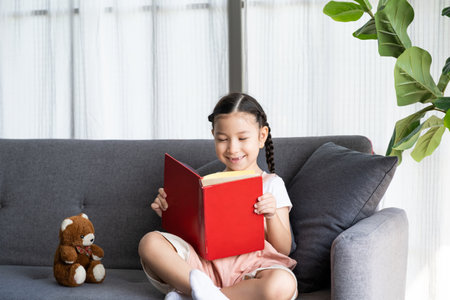 Young Caucasian girl play and reading fairy tale book while have fun with teddy bear doll and her toy in side of the living room. Children enjoyment lifestyle.の写真素材