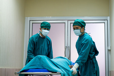 Selective focus at face of the doctor while moving out the body of pass away patient while doctor covering face inside of the surgery operation room in the hospital. Illness and death concept.の写真素材