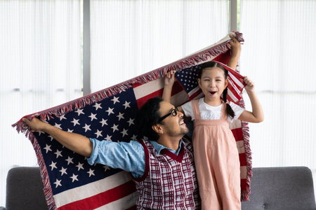 Father and daughter raise and holding American flag and celebrate United State independence date inside of the living room. Shoe feeling of happiness and joyful. Family holiday event.の写真素材
