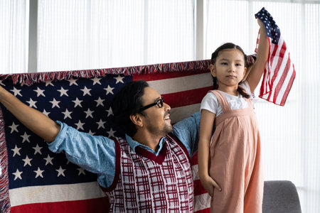 Father and daughter raise and holding American flag and celebrate United State independence date inside of the living room. Shoe feeling of happiness and joyful. Family holiday event.の写真素材