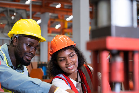 African mechanical engineer team, wearing safety equipment. While doing machine maintenance and safety control while work inside of factory area. With blurred background of heavy machine.の写真素材