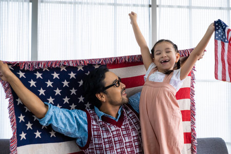 Father and daughter raise and holding American flag and celebrate United State independence date inside of the living room. Shoe feeling of happiness and joyful. Family holiday event.の写真素材