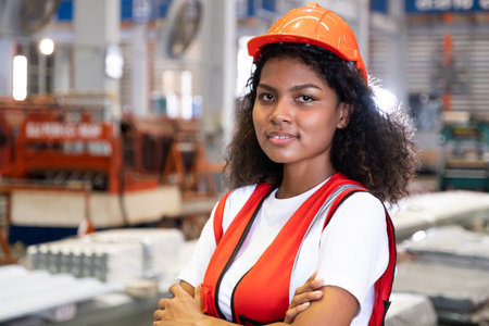 African women mechanical engineer, wearing safety equipment. While do safety control while work inside of factory area. with heavy production machine inside factory at the background.の写真素材