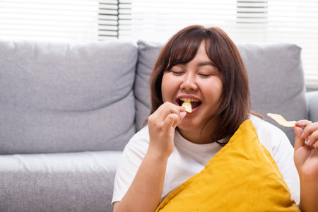 Young Asian oversize women gain weight while eating fried chicken, potato chips and French fried. Junk food that can cause obesity and unhealthy for human body.の写真素材