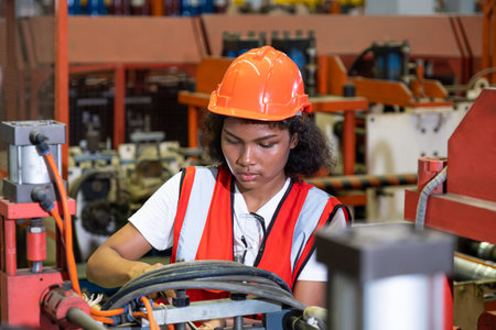 African women mechanical engineer, wearing safety equipment. While do safety control while work inside of factory area. with heavy production machine inside factory at the background.の写真素材