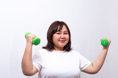 Young Asian chubby woman hold dumbbell for exercise and weight training. Fighting while diet during weight loss program with positive emotion. Portrait shot on white background.の写真素材