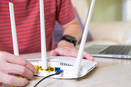 Selective focus at router. Internet router on working table with blurred man connect the cable at the background. Fast and high speed internet connection from fiber line with LAN cable connection.の写真素材