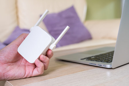 Selective focus at range extender. Internet router on working table with blurred man connect the cable at the background. Fast and high speed internet connection to cover home network usage.の写真素材