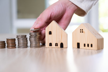 Selective focus Men hand putting coin on stack of money coin for saving for home, property with small wood house on the background. Wealth and saving plan for house mortgage, personal investment.の写真素材