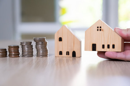 Men hand hold, giving wood house beside increasing money, coin stack on wood table. Saving plan to buy property, house. Personal financial concept for own a house. with copy space for textの写真素材