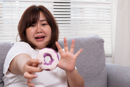 Young plus size Asian women stop herself from eating donut to control body weight during diet period. Healthcare and body weight control to prevent overweight, diabetes and obesity.の写真素材