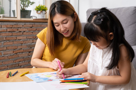 Young Asian girl feeling fun and happy while drawing color paint with her mother or teacher inside...