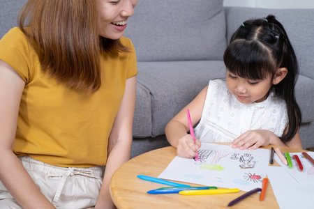 Young Asian girl feeling fun and happy while drawing color paint with her mother or teacher inside of the living room. Family relationship and learning art activity, togetherness and bonding.の写真素材