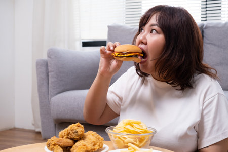 Young Asian oversize women gain weight while eating fried chicken, potato chips and French fried. Junk food that can cause obesity and unhealthy for human body.の写真素材