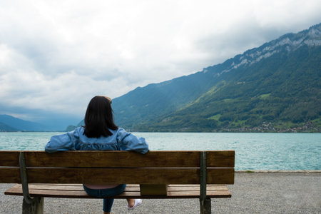 Young Asian tourist women sitting on a bench beside the lagoon while enjoy travel in Iseltwald Switzerland. Tourist attraction view point with copy space.の写真素材