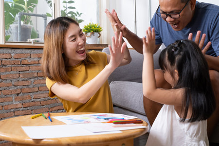 Young Asian girl feeling fun and happy while drawing color paint with her mother and father inside of the living room. Family relationship and learning art activity, togetherness and bonding.の写真素材